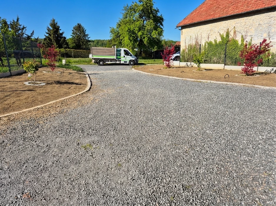 Allée de jardin fraîchement aménagée en graviers concassés gris, bordée de massifs en terre brune avec jeunes arbustes à feuillage rouge