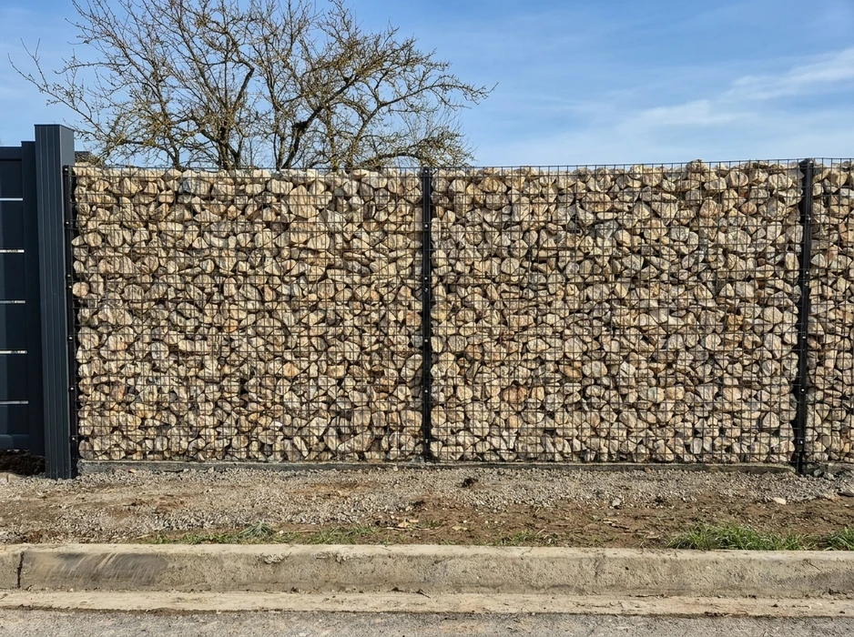 Mur de clôture extérieur en gabions, constitué de deux panneaux métalliques à mailles carrées noires, remplis de pierres calcaires beiges de gros calibre
