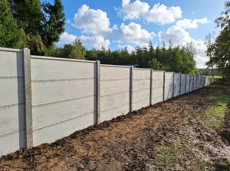 Clôture préfabriquée en béton, posée en extérieur le long d'un terrain boueux
